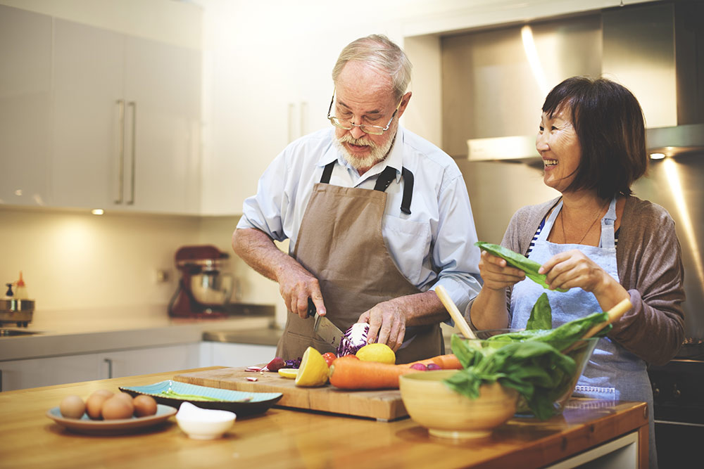Senior couple making healthy dinner in kitchen smiling