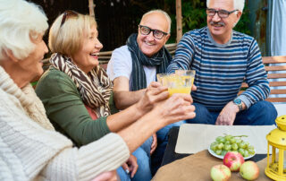 Group of seniors sitting outside eating and drinking together, having fun in senior living community