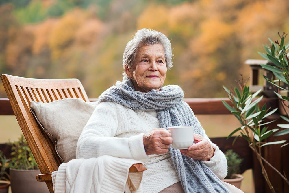 Senior woman sitting outside drinking cup of coffee in assisted living facility