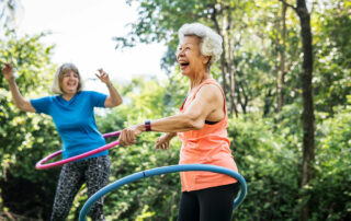 Happy senior women exercising, hula hooping outside