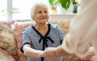 Senior woman smiling looking up at caregiver who is holding her hands