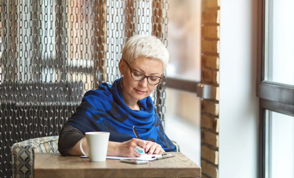 A senior woman writes in her journal in a cafe