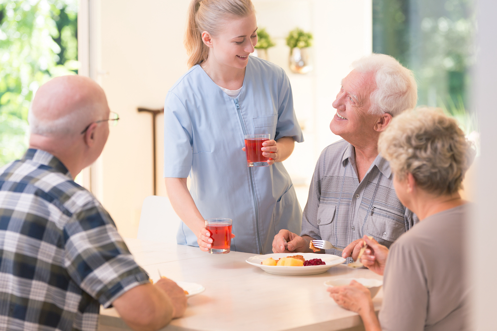 A memory care staff member serves breakfast to seniors
