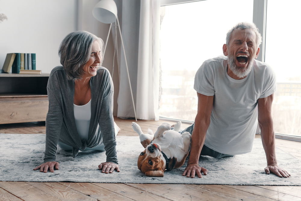 A senior couple laughs while doing yoga because their beagle interrupts 