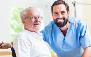 A male caregiver and a senior man smile and talk