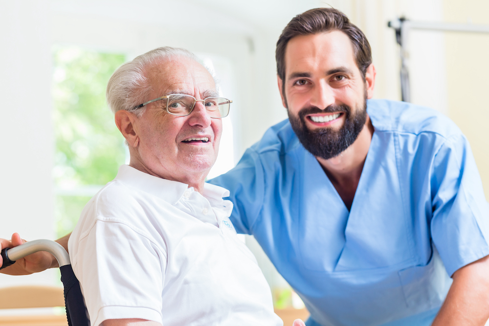 A male caregiver and a senior man smile and talk