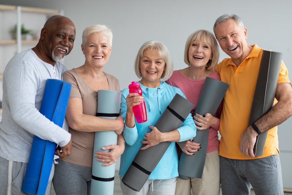A group of active seniors holding yoga mats and chatting