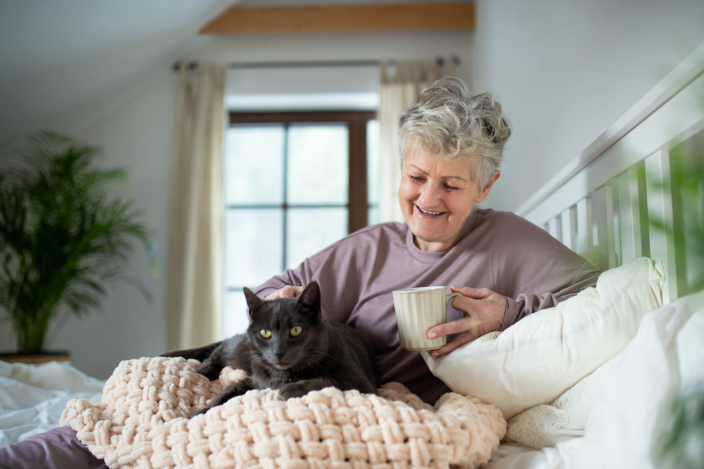 A smiling senior woman drinks tea and pets her cat