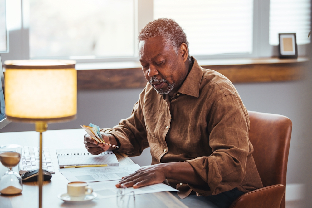 A senior man sits at his desk to see if he can afford one of the senior living homes in his area