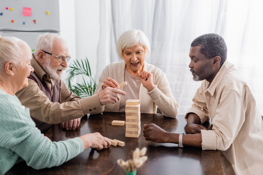 A group of four senior friends playing a board game at their senior living communities