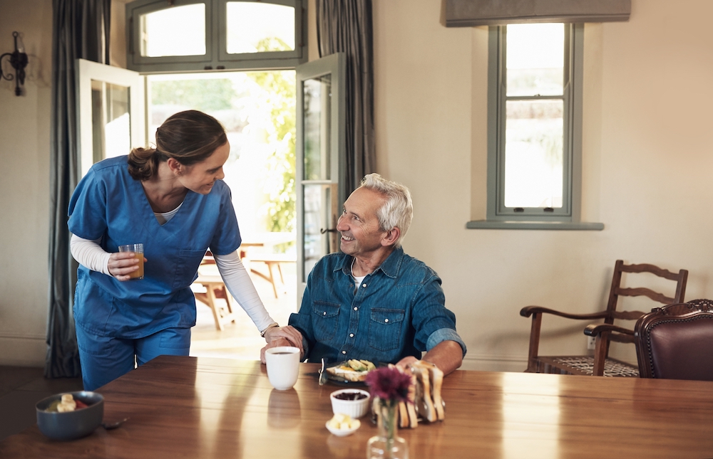 A memory care nurse bringing a resident a cup of coffee at breakfast
