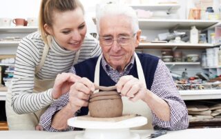 A woman helping a senior man at a pottery class