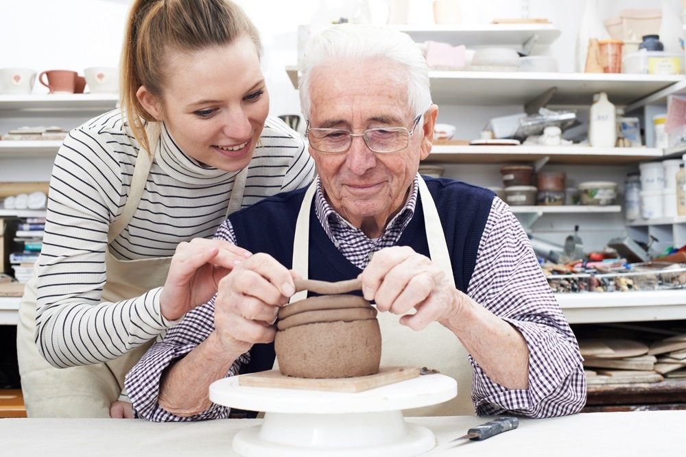 A woman helping a senior man at a pottery class