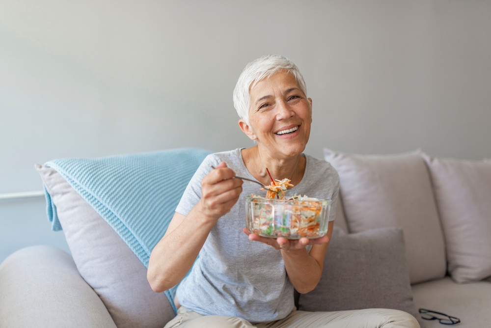 A happy senior woman sitting and eating a healthy salad