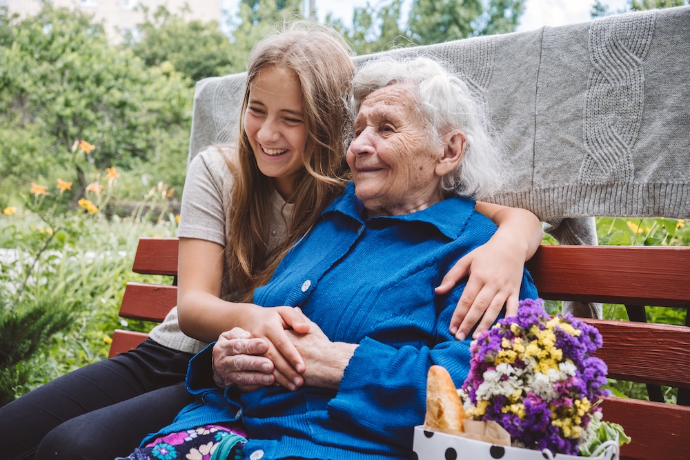 Grandmother with her granddaughter outside her memory care program sitting on a bench in the garden