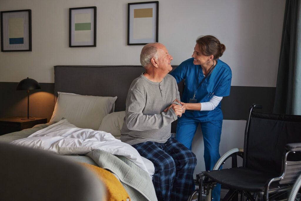 Awake overnight memory care team member gently assisting a resident in a softly lit community hallway